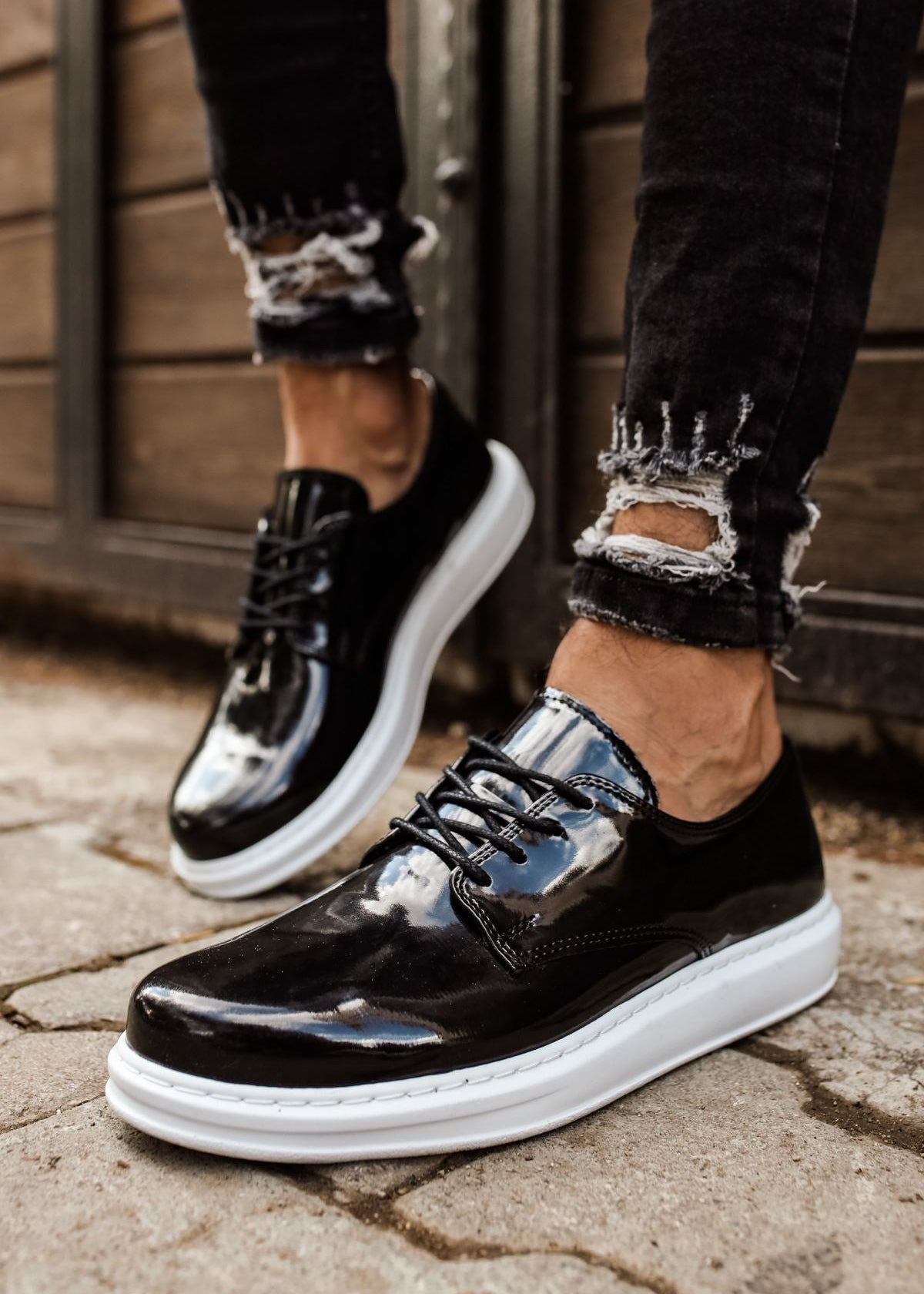 Black patent leather shoes with white soles worn on a stone pavement.