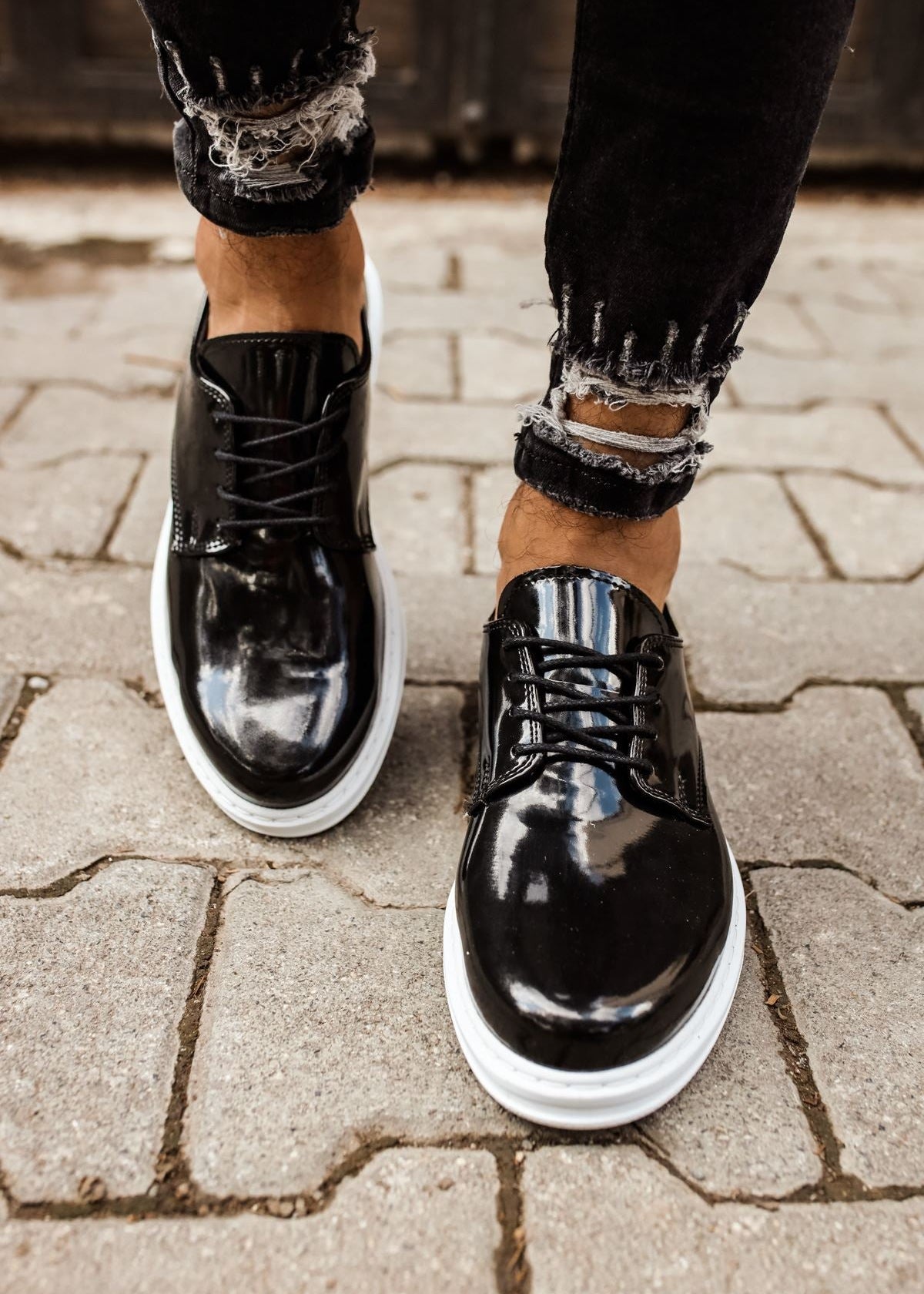 Black shiny shoes with white soles worn on a paved surface