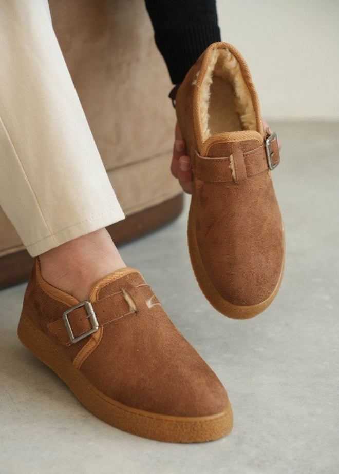 Brown suede shoes with buckles worn by a person on a light background