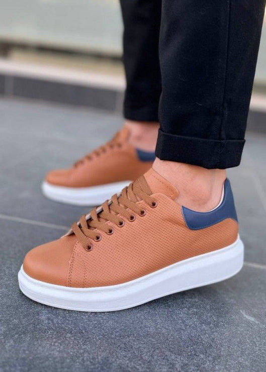 Brown sneakers with a blue accent worn by a person on a tiled floor.