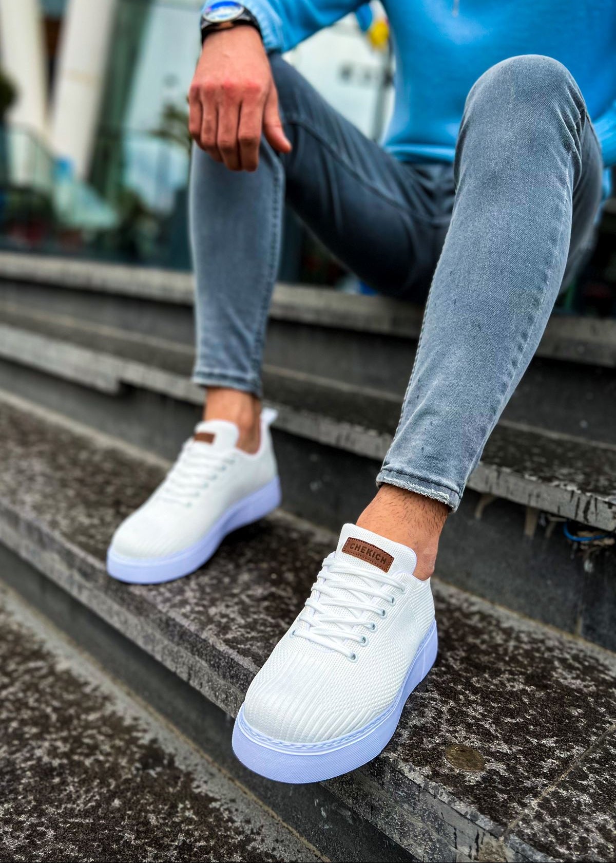 Person wearing white sneakers and blue jeans sitting on steps.