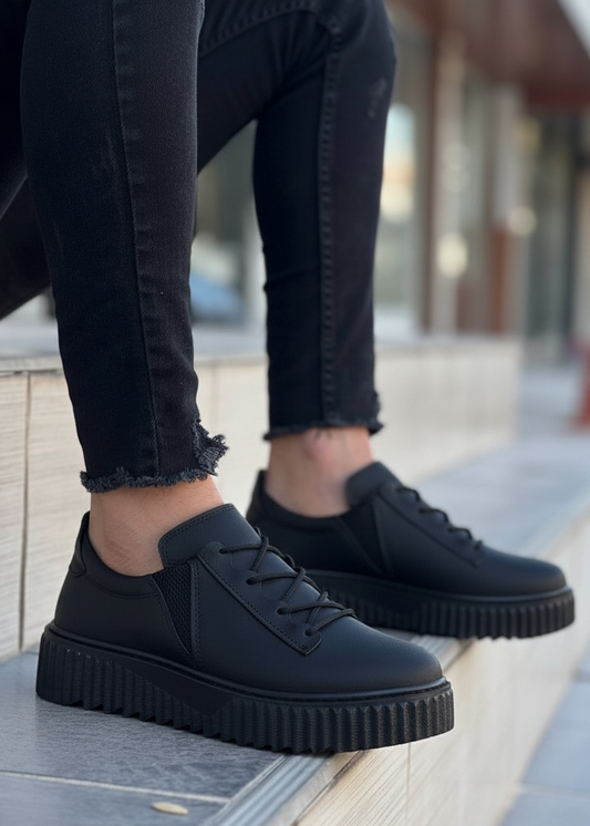 Person wearing black platform shoes and black jeans sitting on a ledge.