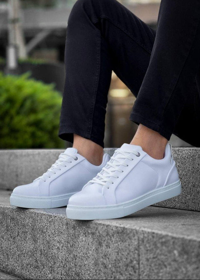 White sneakers worn on a person sitting on concrete steps with a blurred green background