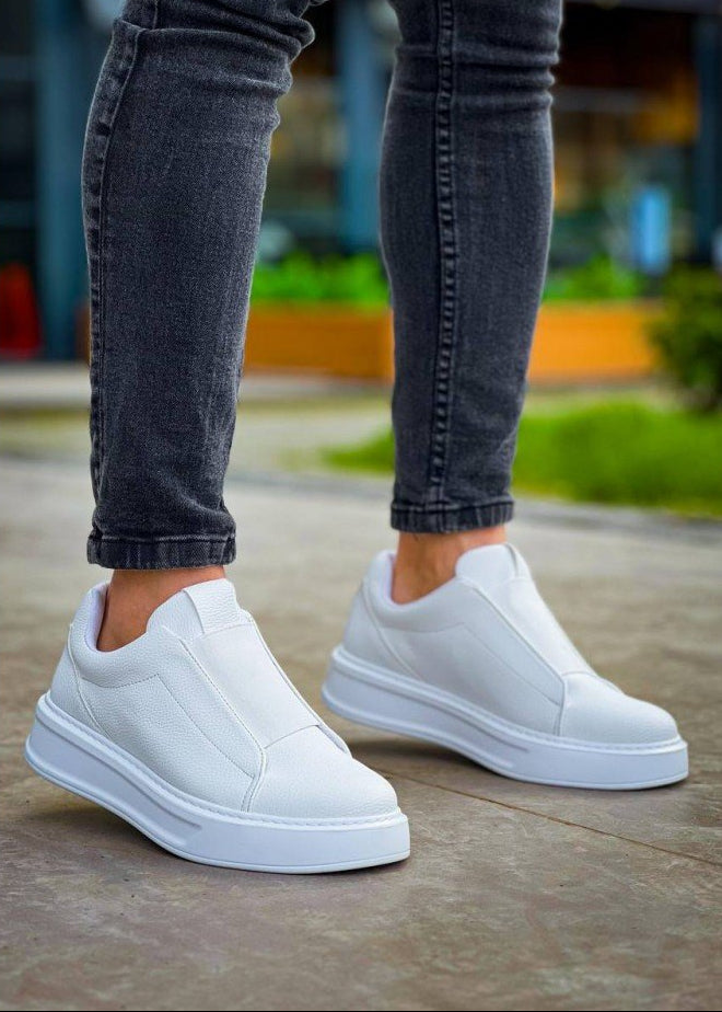 White slip-on sneakers worn with dark jeans on a concrete surface.