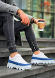 White sneakers with blue accents worn by a person sitting on steps, holding a coffee cup.