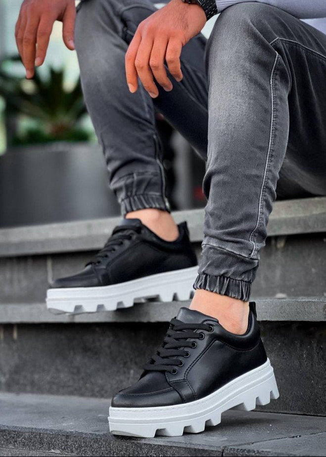 Person wearing black sneakers with white soles on a concrete surface