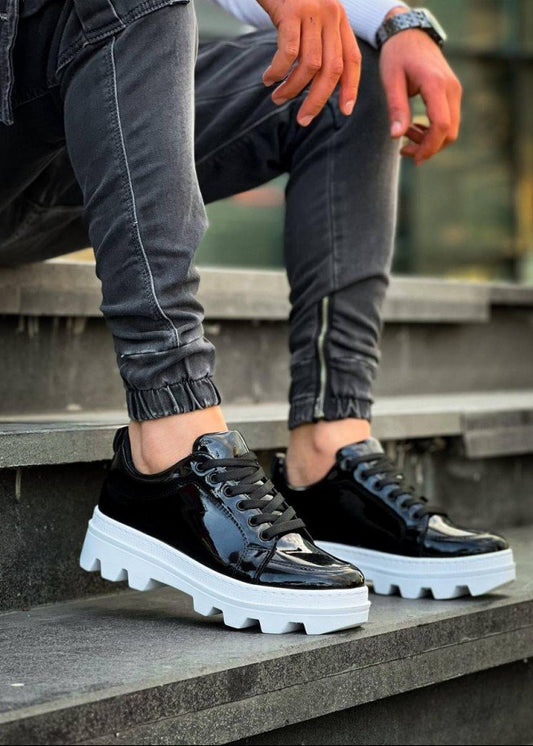 Black glossy sneakers with white soles worn by a person sitting on steps.