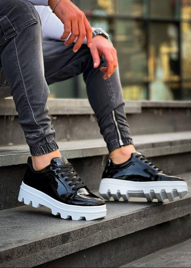 Black patent leather sneakers with white soles worn by a person on stone steps.