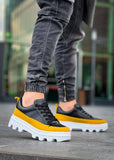 Black and yellow sneakers with white soles worn by a person on a blurred background