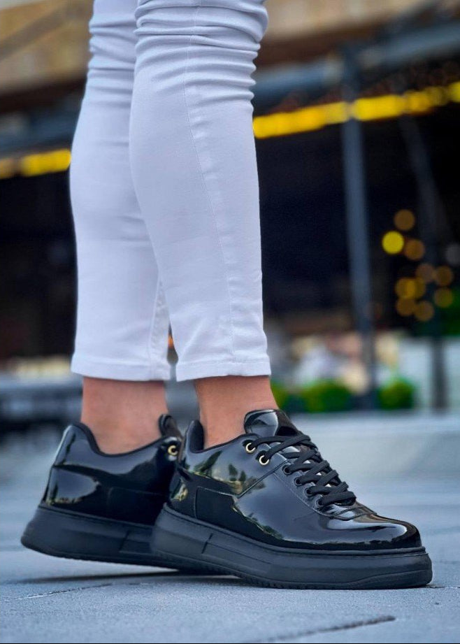Black patent leather shoes worn with white pants on a blurred outdoor background